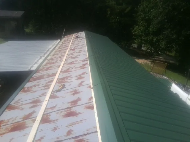 Old rusted panels beside newly installed green metal roofing — Wind Damage Roof Repair by Roofing Brothers in Blairsville
