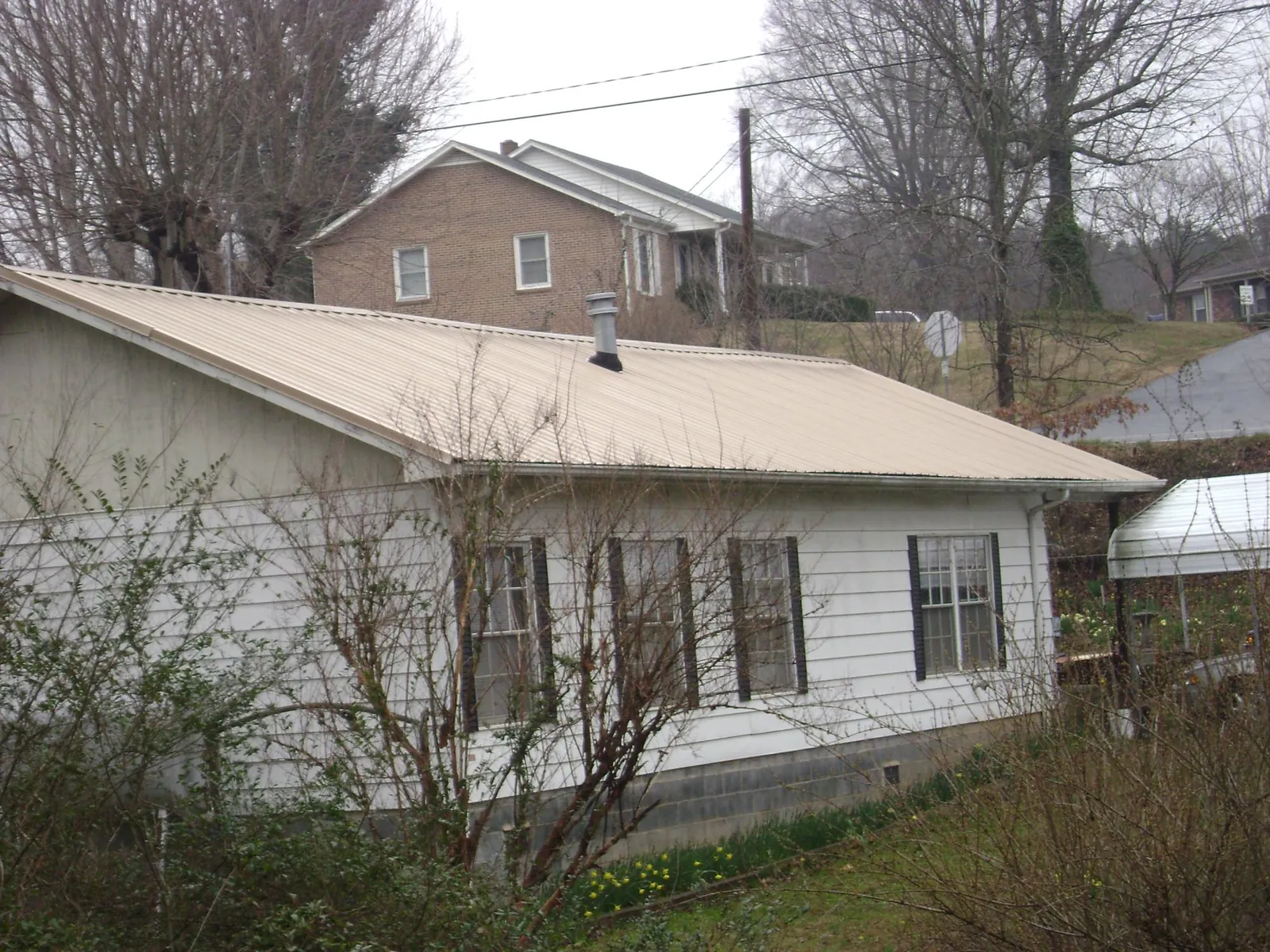 Tan metal roof on a white sided house set into a hillside — Commercial Roofing by Roofing Brothers in Blairsville